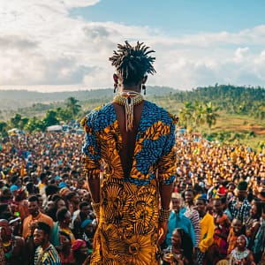 A performer in colorful attire captivates a large crowd at a tropical Afrobeat music festival.